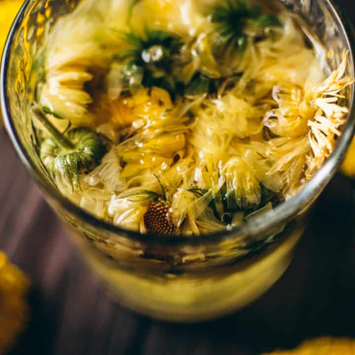 A glass of calendula tea with yellow flowers in it.