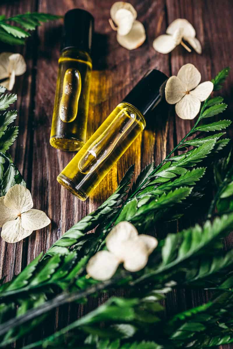 A dark wood table topped with green plants, dried flowers and small glass bottles filled with yellow oil.