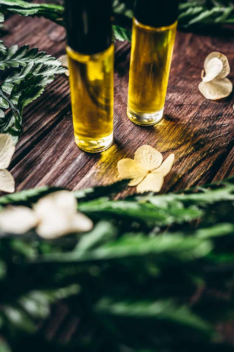 Two small clear glass bottle filled with yellow oil lit by the sun.