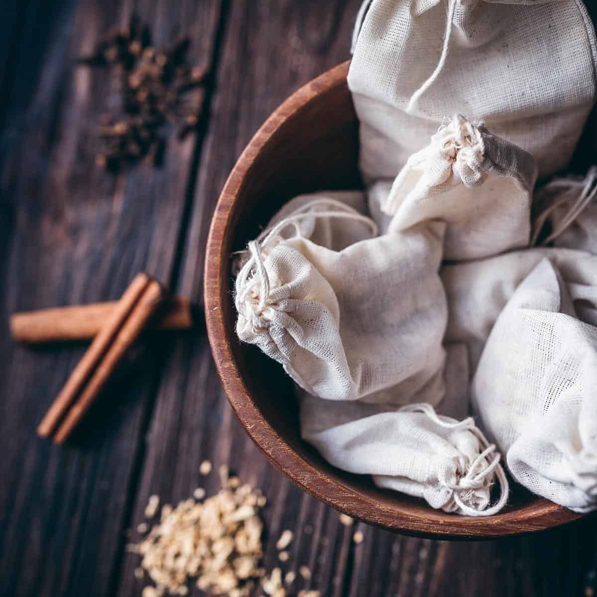 A wooden bowl filled with white muslin bags that are tied shut.