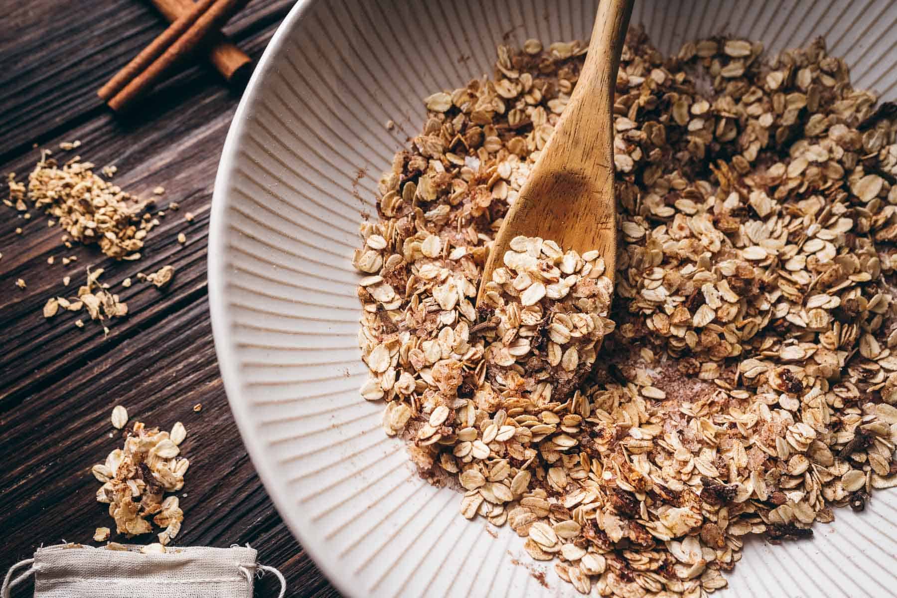 A white ceramic bowl filled with oats and brown ground spices rests on a dark wooden tabletop.