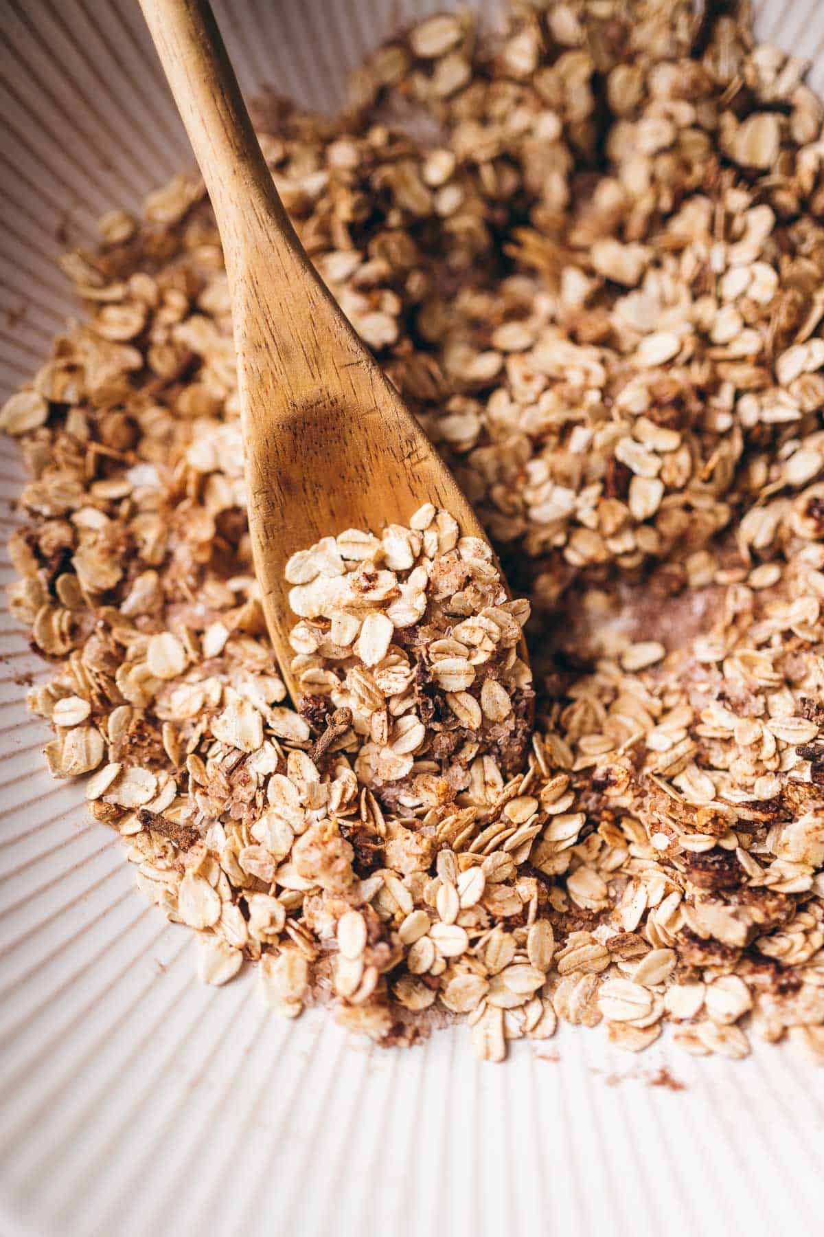 A wooden mixing spoon rests in a white bowl of rolled oats.