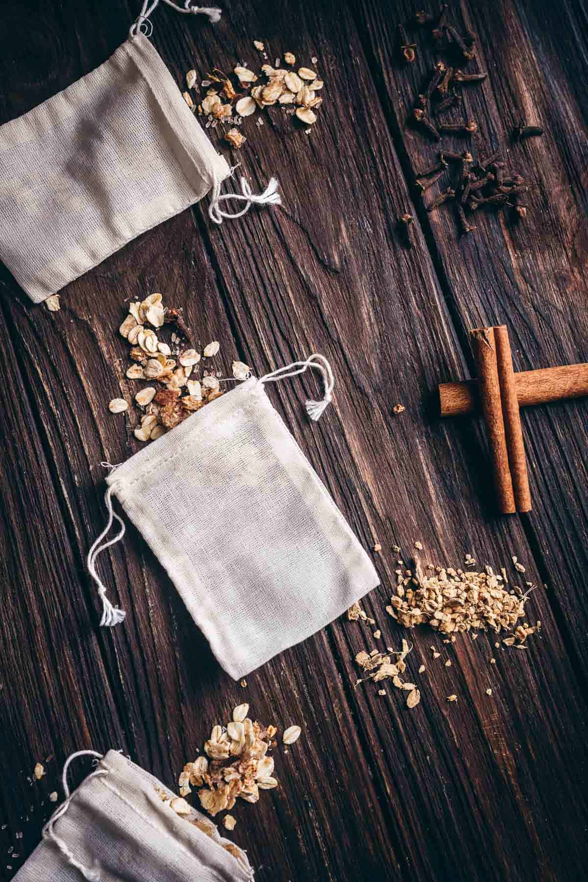 White muslin bags, oats and spices rest on a dark wooden table.