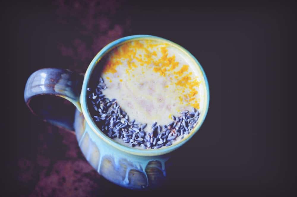 A green ceramic mug filled with a white liquid and topped with small, dried purple flowers.