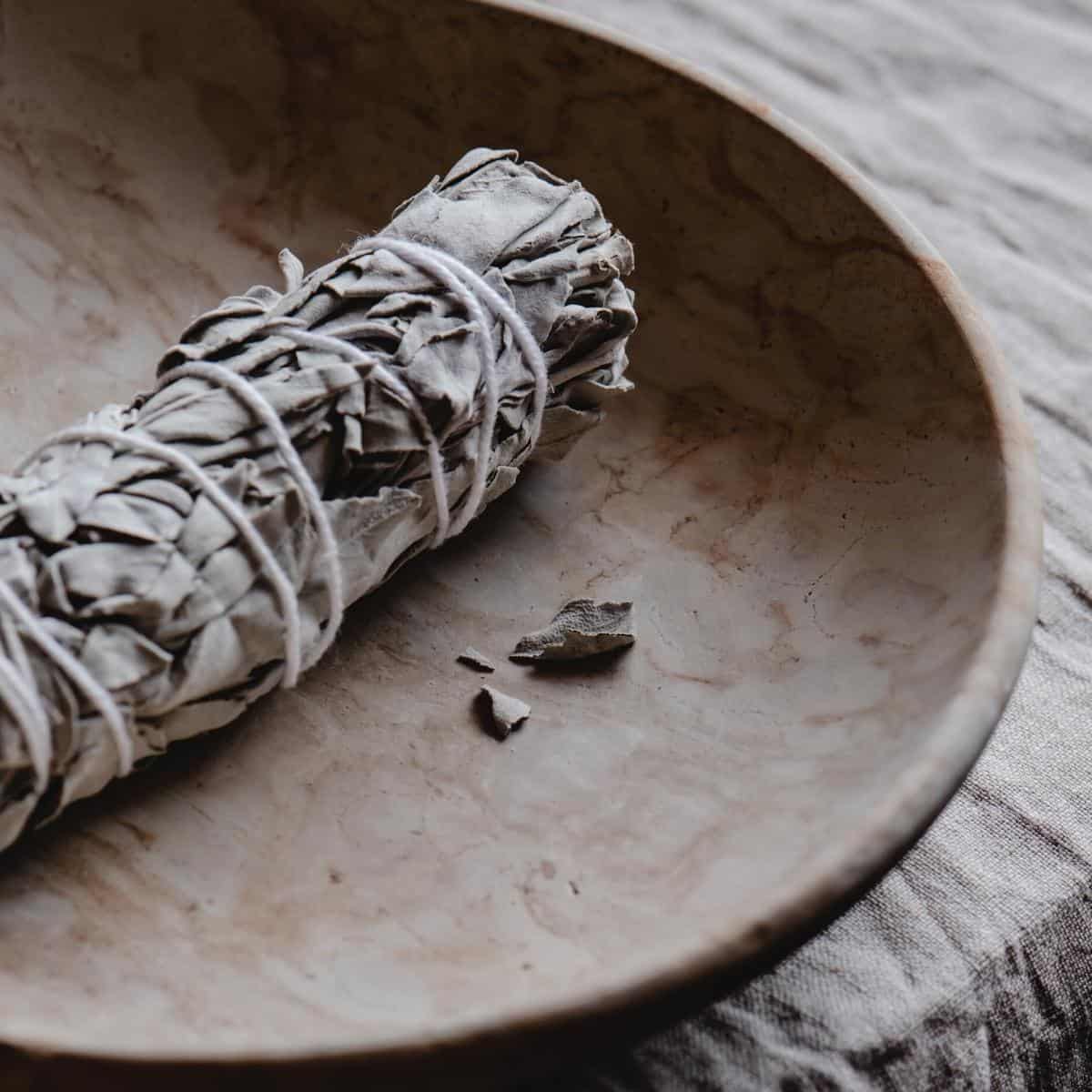 Dried white sage leaves wrapped with white string resting in a ceramic dish.