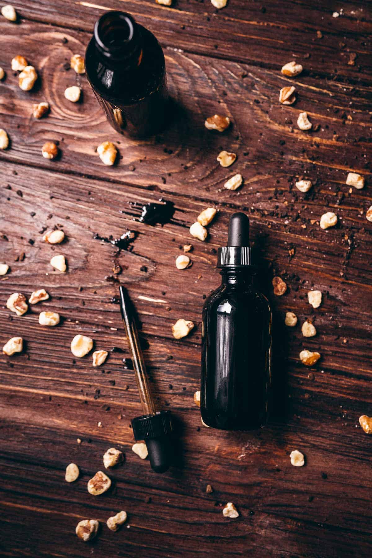 Top view of dark tincture bottles resting on a wooden table sprinkled with walnuts.