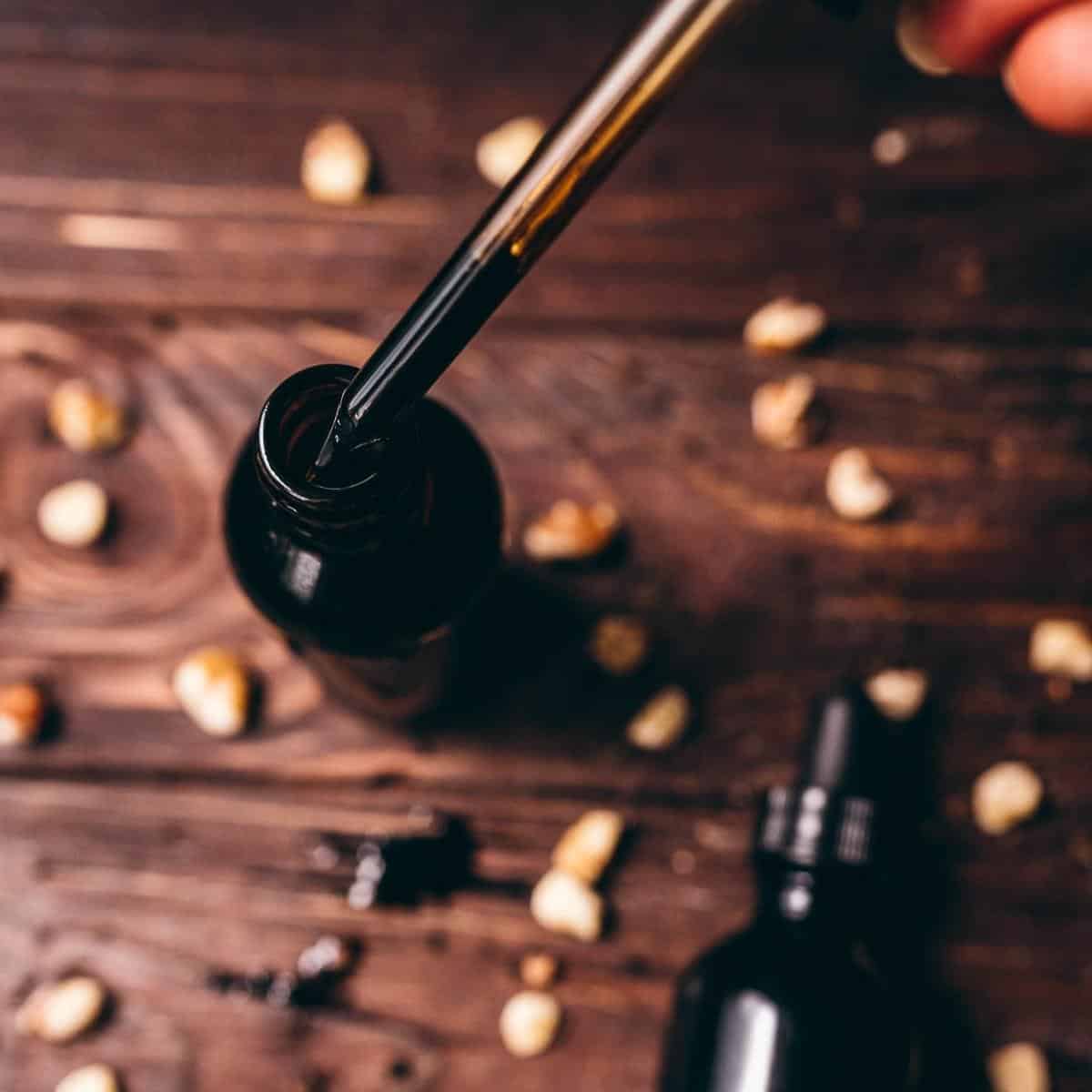 A hand holding a dropper bulb over a dark glass bottle.