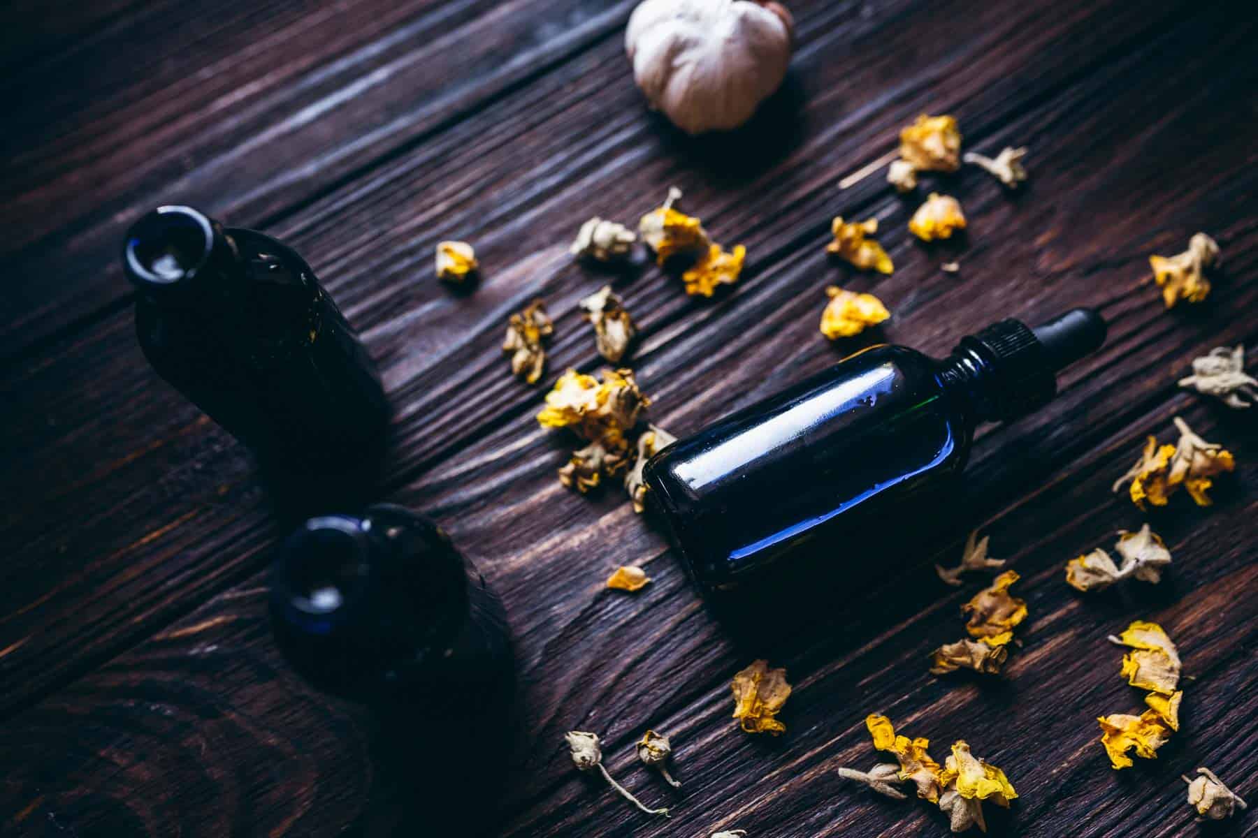 A blue glass dropper bottle resting on a dark tabletop scatter with small dried yellow flowers.