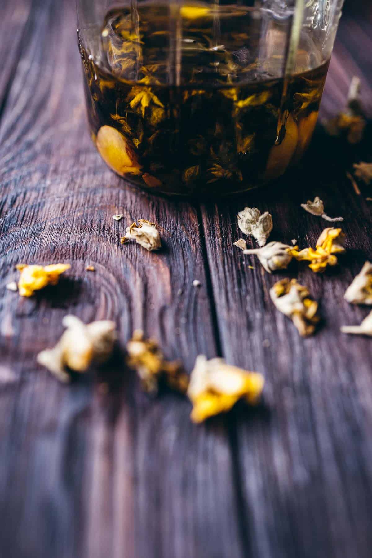 A clear glass jar filled with oil, garlic and flowers rests on a dark tabletop.