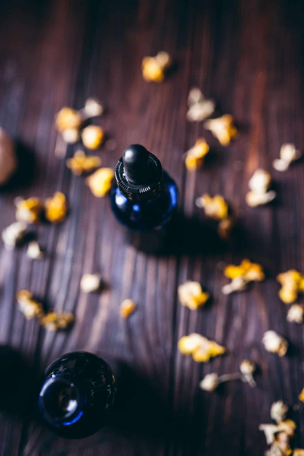 A blue dropper bottle rests on a wooden table scattered with yellow flowers.