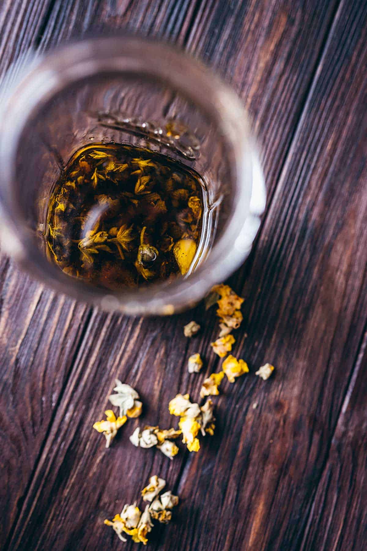 An open glass jar filled with oil and yellow mullein flowers.