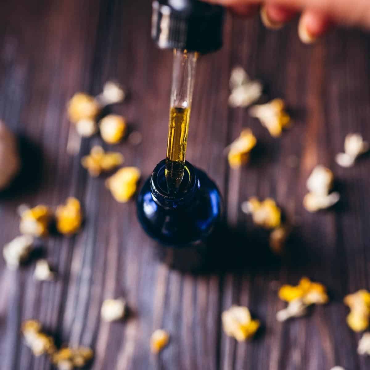 A dropper bulb filled with yellow oil being pulled out of a small blue glass bottle.