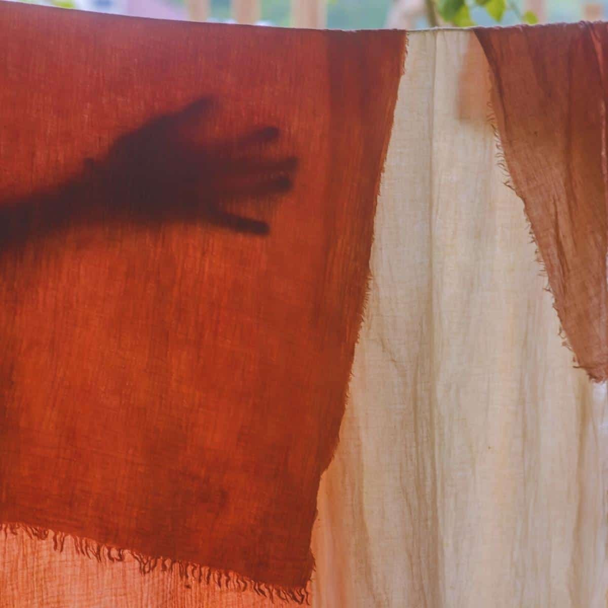 The silhouette of hand behind naturally dyed fabric hanging from a clothes line.