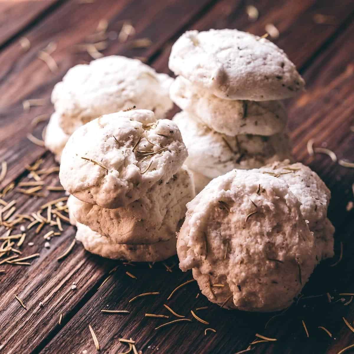 White bath truffles resting on a dark wooden table scattered with dried rosemary.