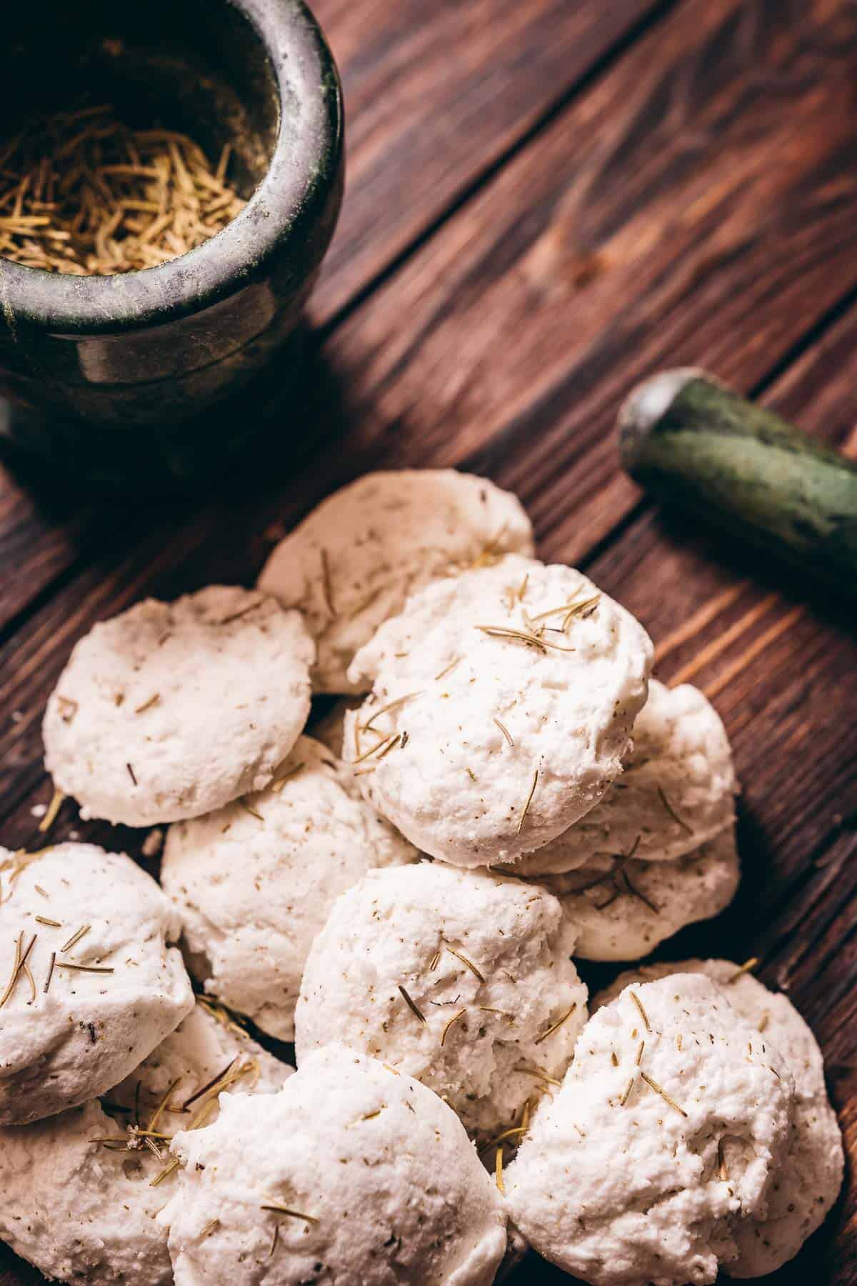 A pile of white homemade bath truffles rest on a dark wooden table.