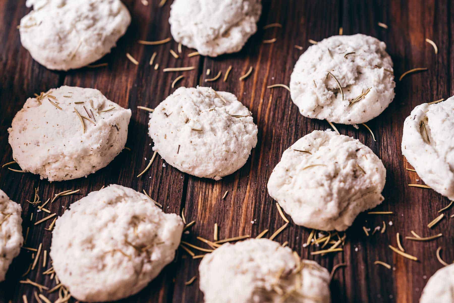 White bath truffles resting on a dark wood table scattered with dried rosemary.