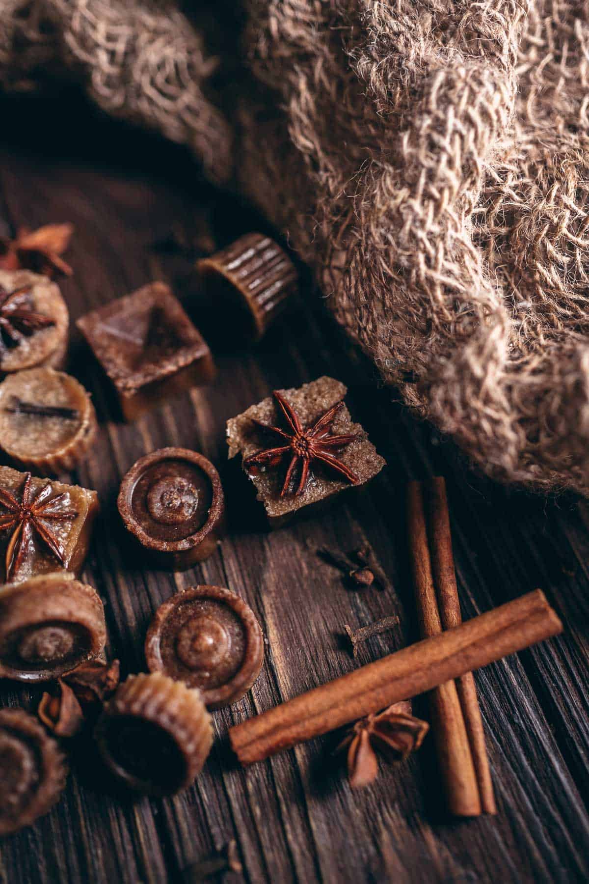 Brown bath melts topped with whole star anise resting on a dark wooden table next to burlap and cinnamon sticks.