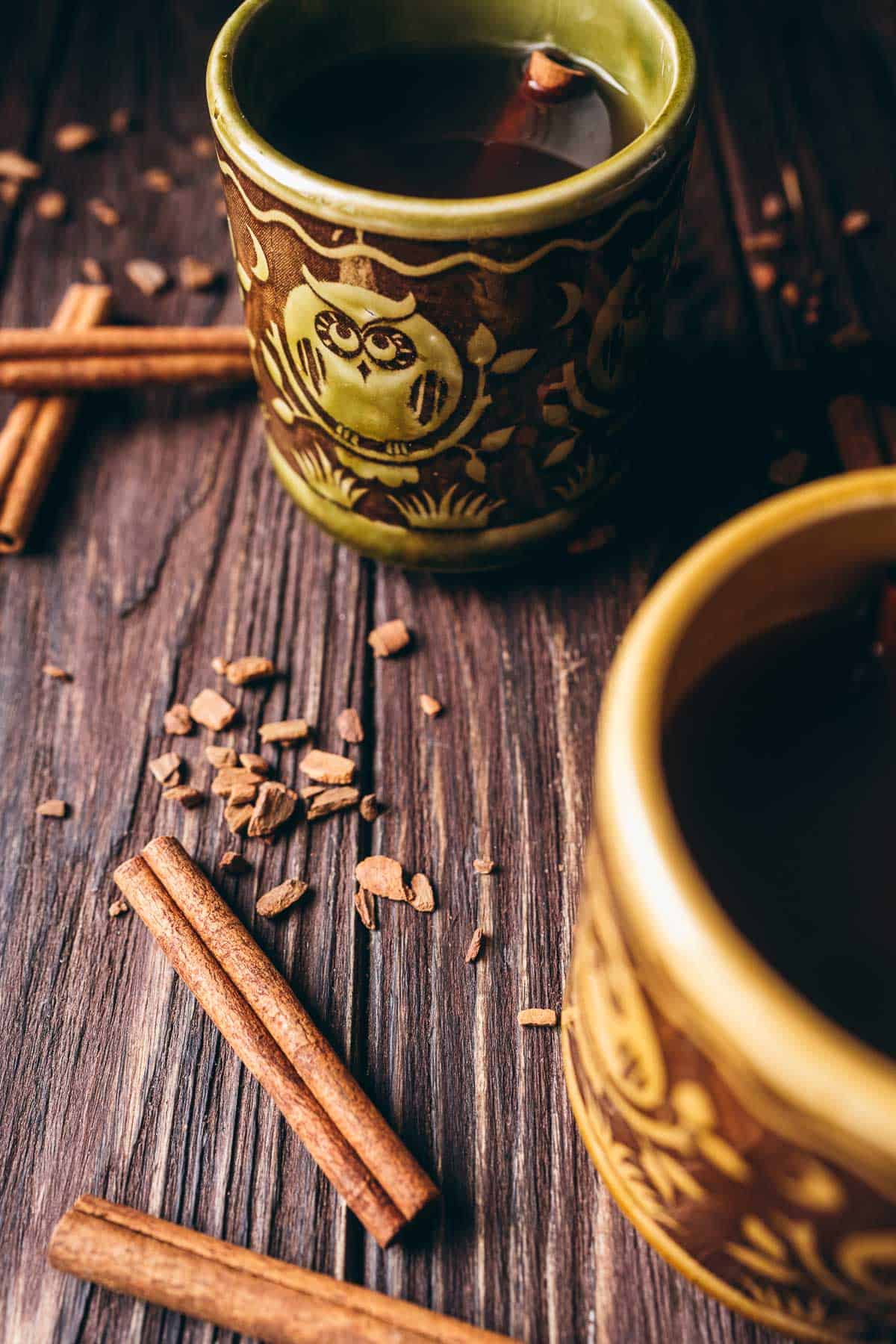 A dark wooden table scattered with cinnamon sticks, cinnamon bark chips.