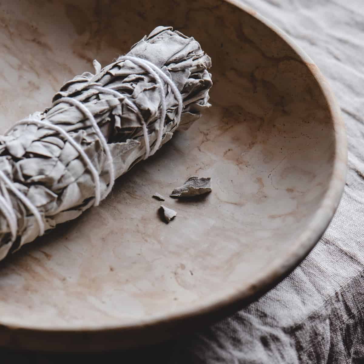 A sage bundle resting in a small tan ceramic bowl.