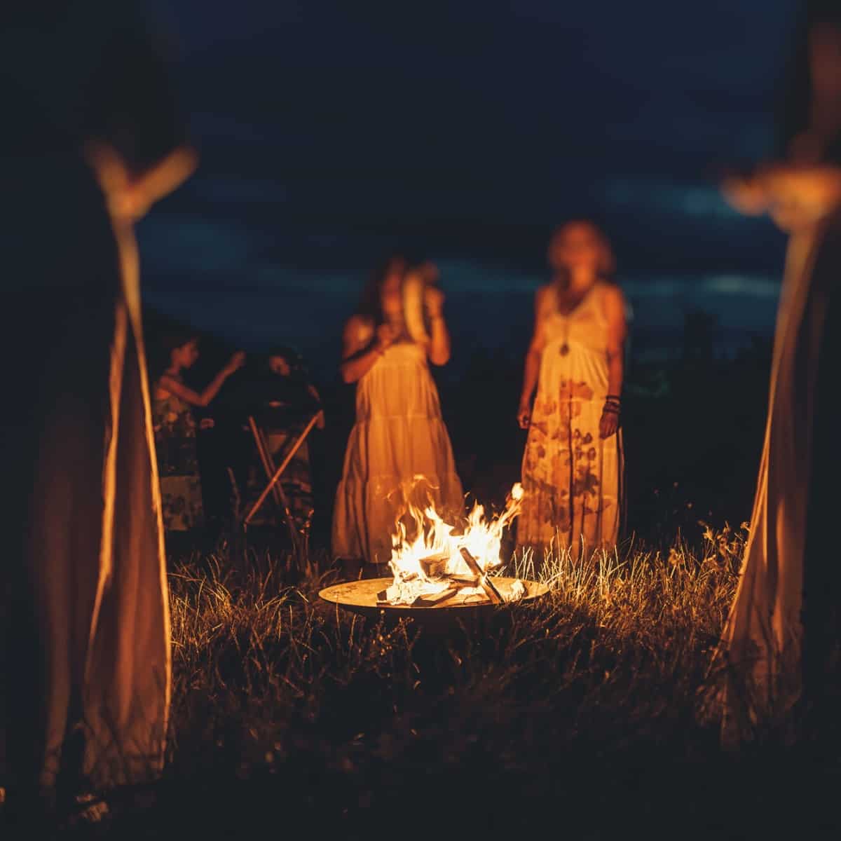 Women in white dresses standing around a fire.