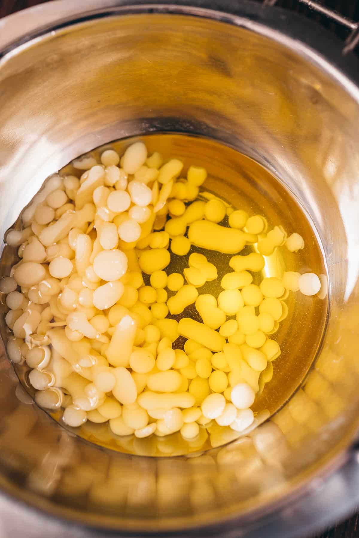 A silver pot filled with partially melted white beeswax pellets.