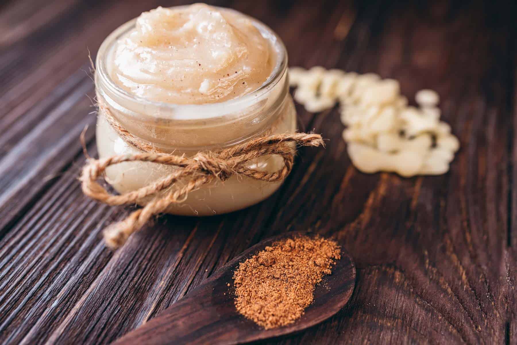 A small glass jar of creamy homemade lotion resting on a dark tabletop.