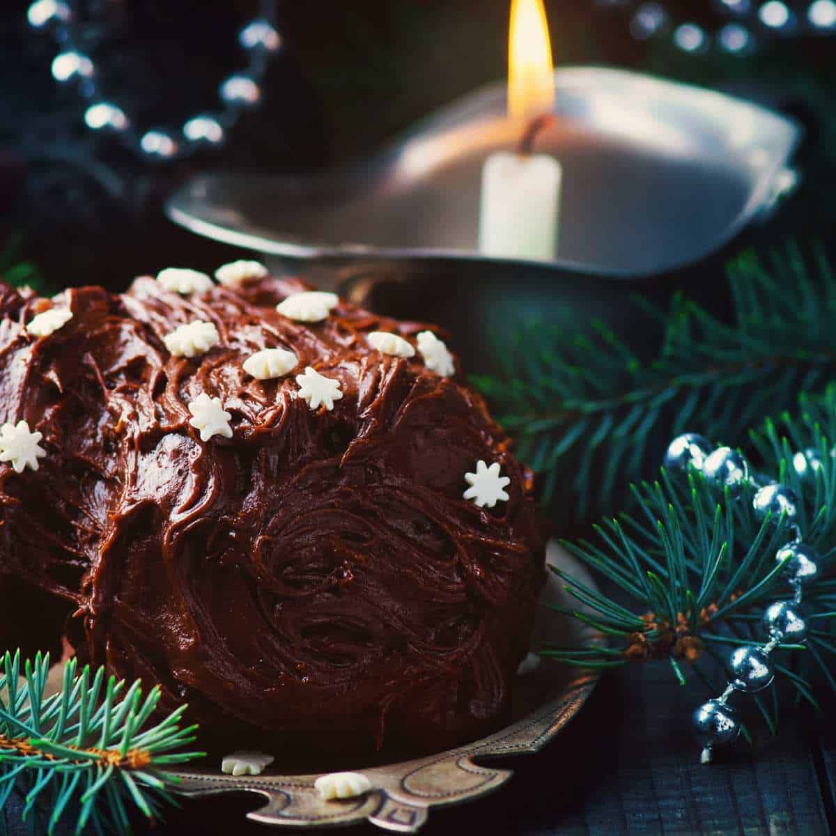 A chocolate cake is sitting on a plate next to a yule candle.