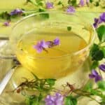 A cup of violet tea with purple flowers adorning it.