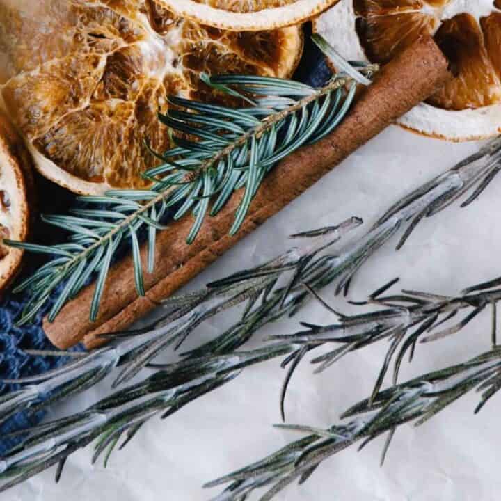 Dried orange slices, a cinnamon stick, and sprigs of rosemary—one of the renowned herbs for prosperity—are artfully arranged on a white surface.