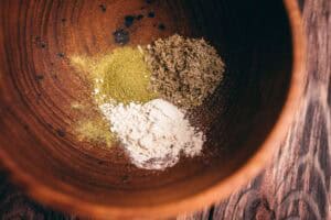 Three piles of different powdered ingredients in a wooden bowl, ready to make incense cones.