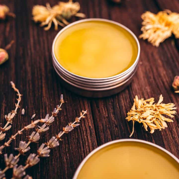 Tin containers with hand salve nestled on a wooden surface, surrounded by dried flowers and herbs.