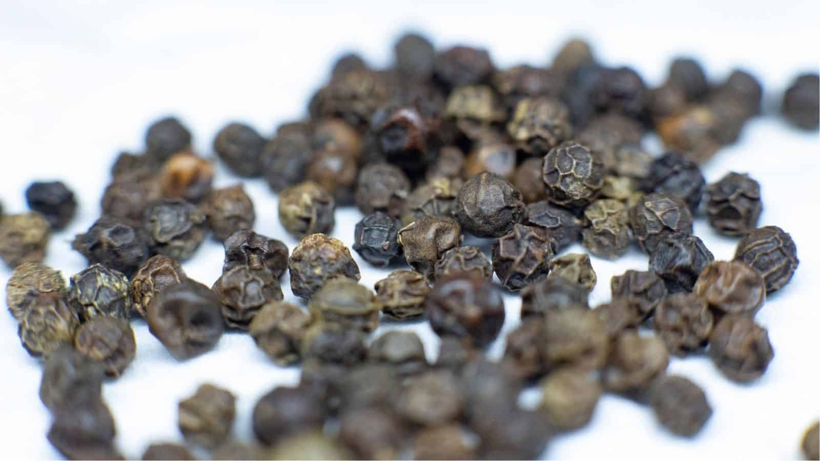 A scattered pile of black peppercorns on a light surface.