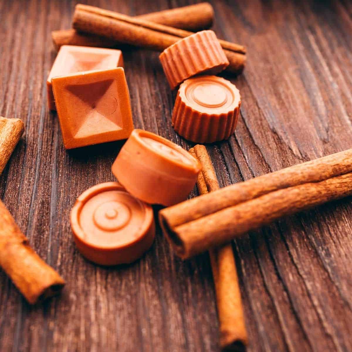 Assorted caramel chocolates and cinnamon sticks on a wooden surface.