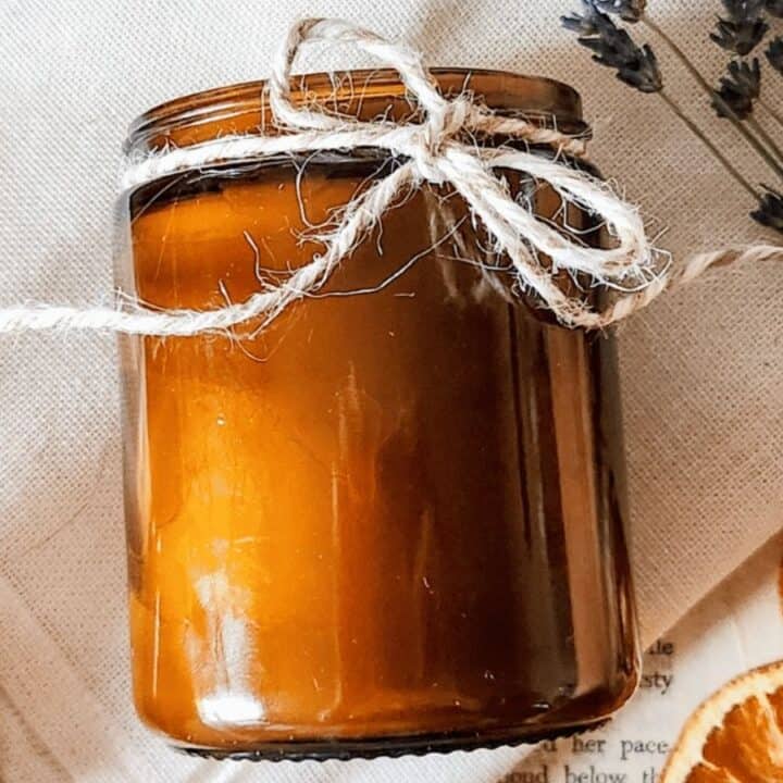 A brown glass jar with twine on top, surrounded by dried orange slices and lavender sprigs on a beige cloth.