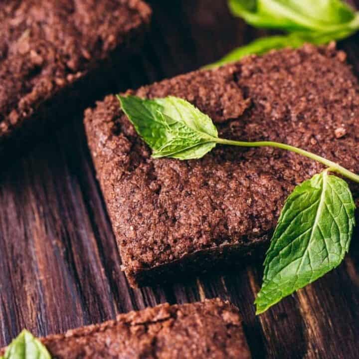 Brownies topped with fresh mint leaves on a wooden surface.