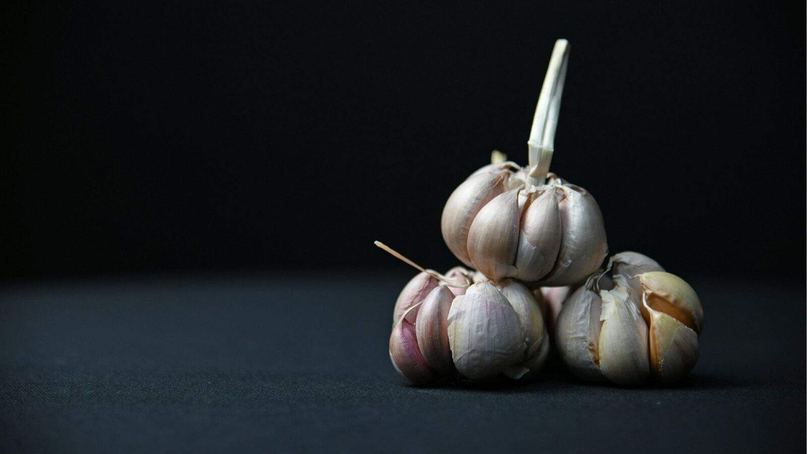 Three heads of garlic stacked on a dark surface with a black background.