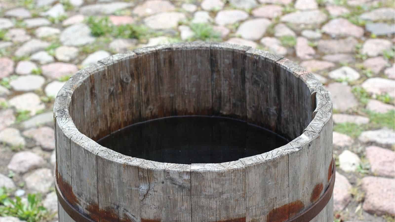 A wooden barrel filled with dark water is placed on a cobblestone surface.