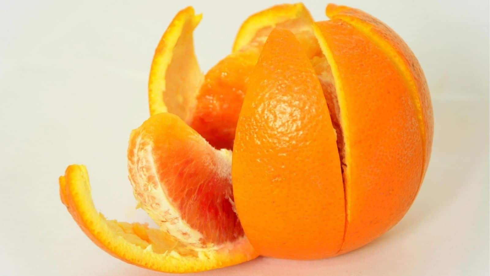 A partially peeled orange with several segments exposed, resting on a white surface.