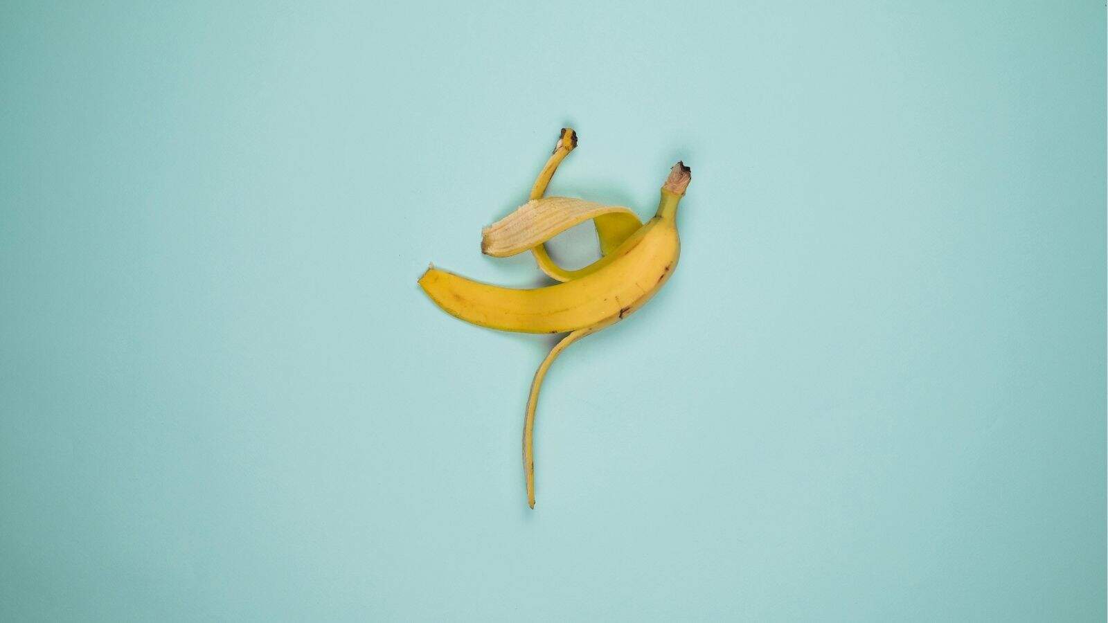 A partially peeled yellow banana lies on a light blue background.
