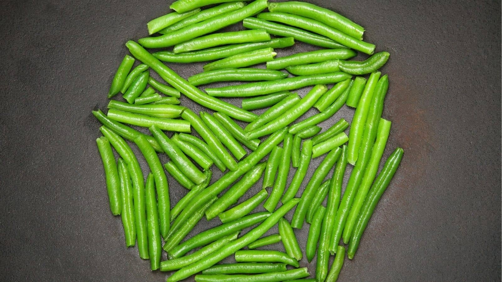 Fresh green beans arranged in a roughly circular pattern on a dark, textured surface.