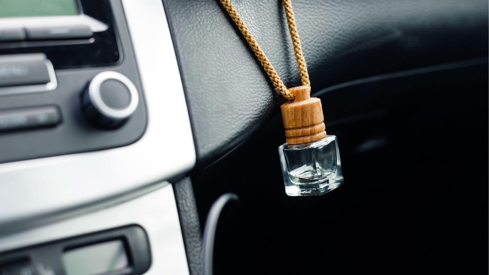 A small glass air freshener with a wooden cap hangs from a cord on a car dashboard near the air vent.