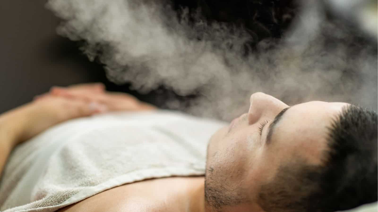 A person lies down with a towel on their chest, receiving a facial steam treatment.