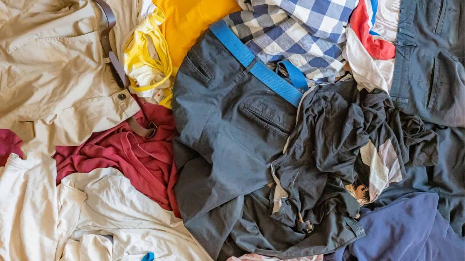 A pile of assorted clothing, including shirts, pants, belts, and mixed fabrics, scattered on a flat surface.