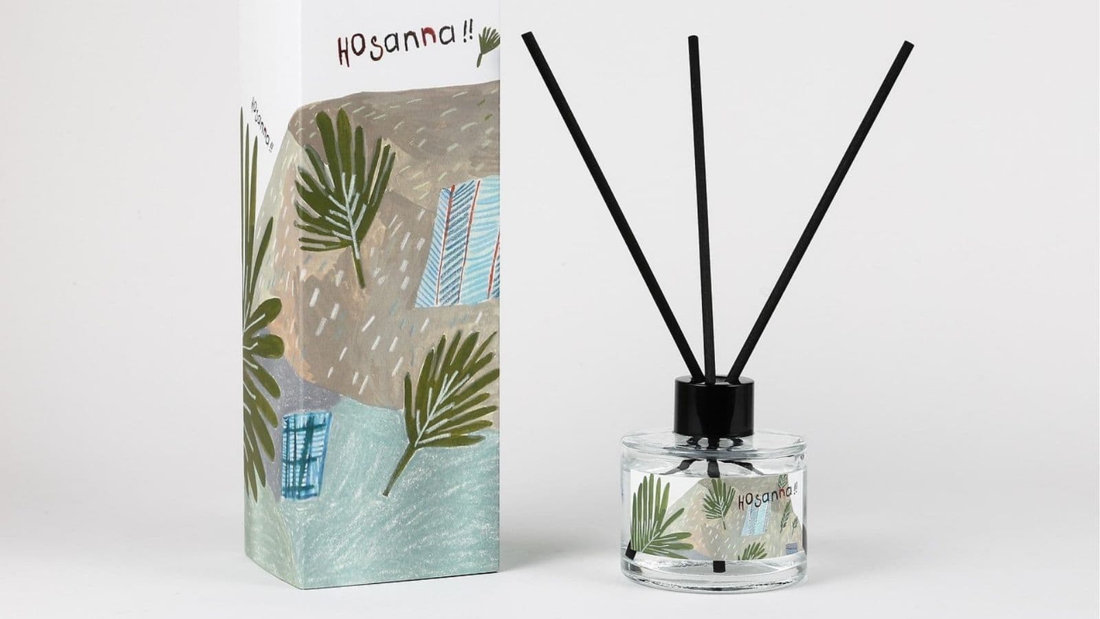 A clear glass reed diffuser with black sticks is placed next to a matching decorative box featuring green palm leaves and abstract patterns. The label and box read "Hosanna!!".