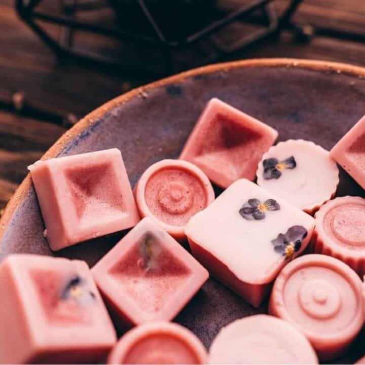 A ceramic bowl filled with assorted pink chocolates, some topped with small dried flowers, sits on a wooden surface.