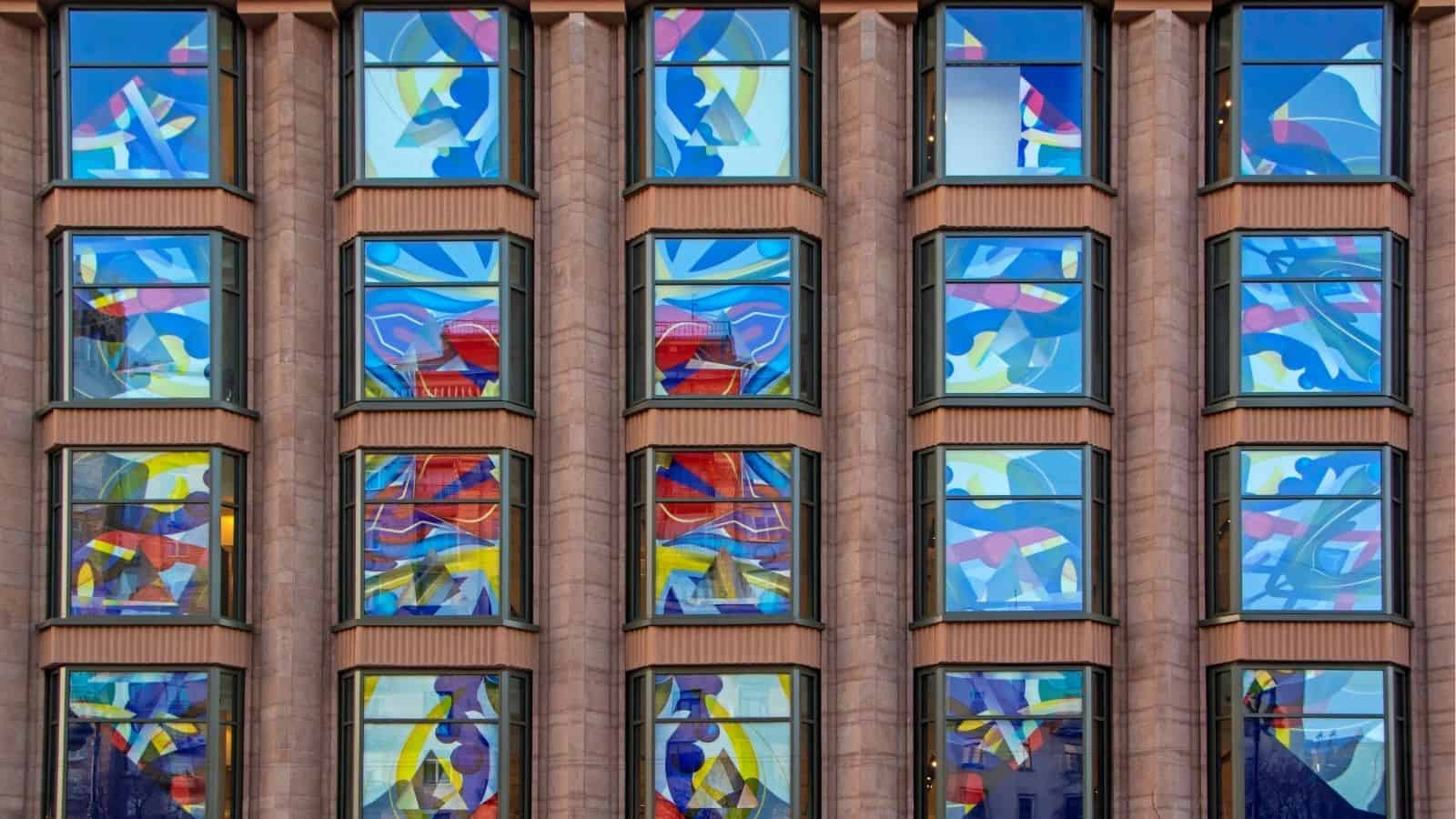 A building facade with large vertical columns and windows decorated with colorful abstract patterns in blue, yellow, red, and white.
