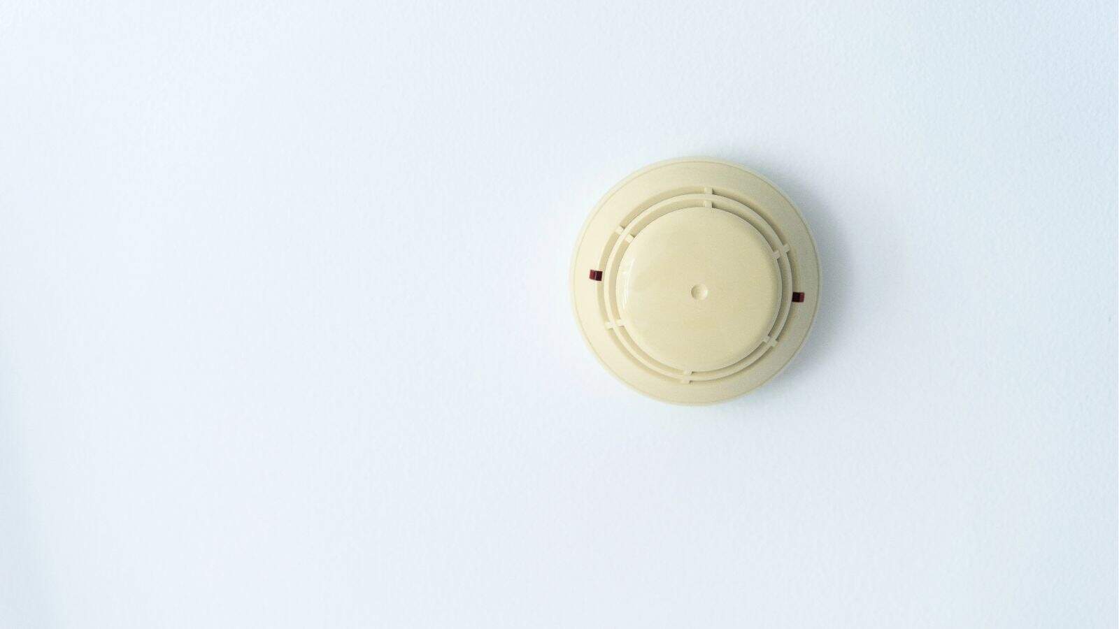 A beige smoke detector mounted on a plain white wall.