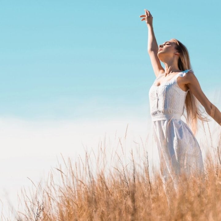 A woman in a white dress standing in a field of tall grass.
