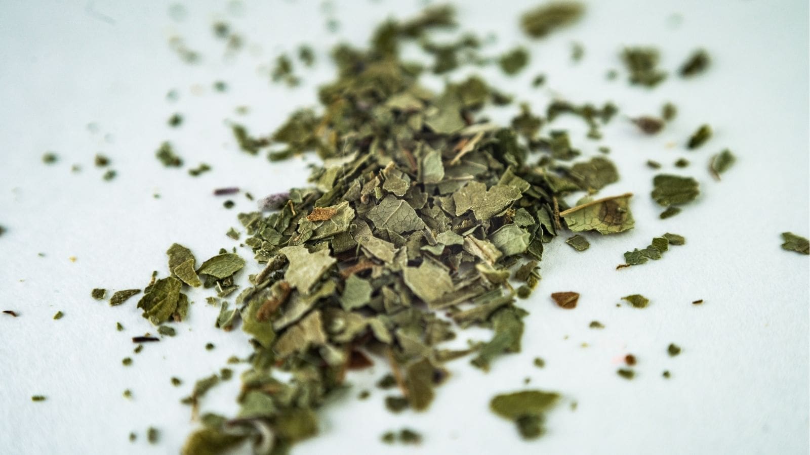 A close-up of dried green leaves, finely chopped and scattered on a white surface.