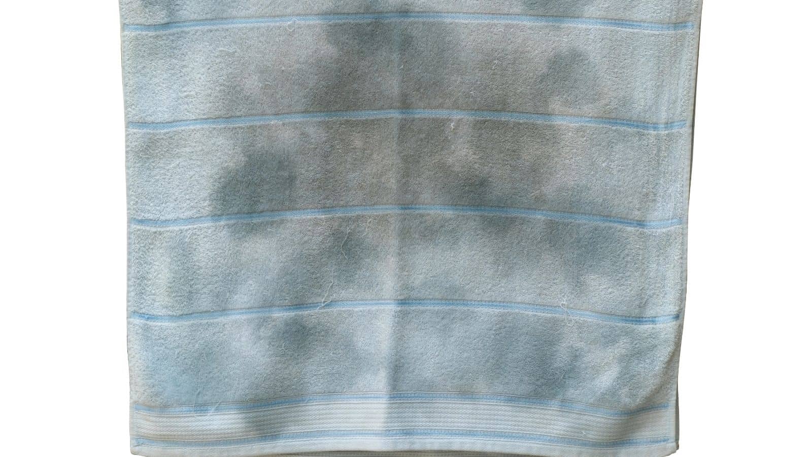 A light blue towel with faint darker patches and horizontal stripes hanging against a plain background.